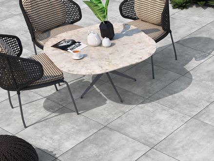 Taras z krzesłami i fotelami, na podłodze jasne płytki z gresu porcelanowego imitujące beton