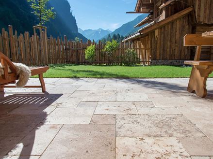 Podłoga tarasu z trawertynu Rustic i drewniane meble, w tle trawnik i widok na góry