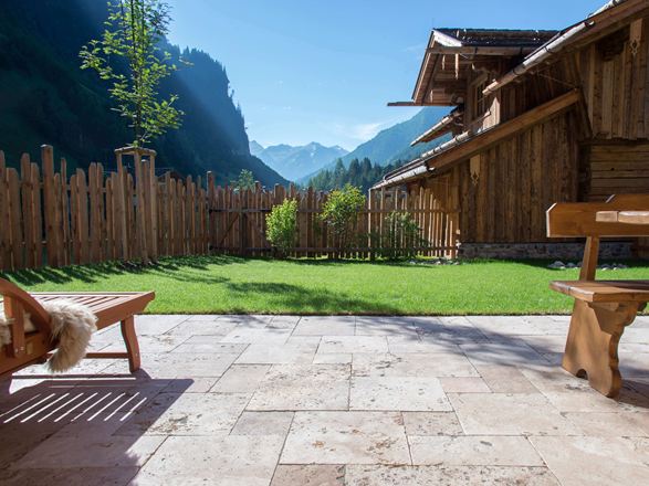 Podłoga tarasu z trawertynu Rustic i drewniane meble, w tle trawnik i widok na góry