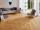 Szara, nowoczesna sofa z fotelem na płytkach z gresu porcelanowego imitujących drewno w kolorze Urban Honey w jasnym salonie