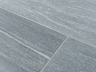 Zbliżenie na płytki z gresu porcelanowego w jasnoszarym wzorze imitującym granit z wąskimi białymi fugami