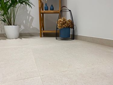 Zbliżenie na podłogę wyłożoną płytkami z gresu porcelanowego Sevilla Cream o wyglądzie wapienia. W tle drewniany regał, roślina i elementy dekoracyjne
