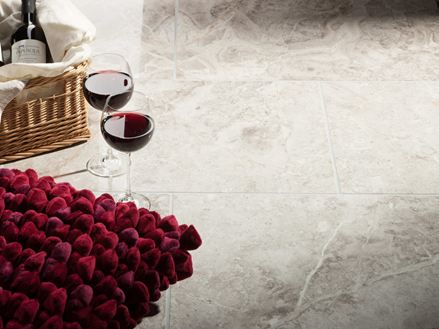 Dwa kieliszki do wina stoją obok koszyka z butelką wina i czerwoną poduszką na wypolerowanych płytkach marmurowych Silver Shadow
