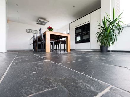 Widok z perspektywy żaby na podłodze z łupków Black Rustic, z drewnianym stołem i rośliną w tle