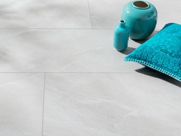 Płytki z gresu porcelanowego w jasnoszarym wzorze imitującym łupek z turkusowym wazonem i turkusową poduszką
