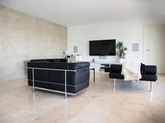 Nowoczesny salon z czarną sofą i jasnobeżowymi płytkami z trawertynu Classic Light jako wykładziną podłogową
