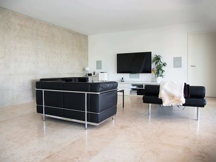Nowoczesny salon z czarną sofą i jasnobeżowymi płytkami z trawertynu Classic Light jako wykładziną podłogową