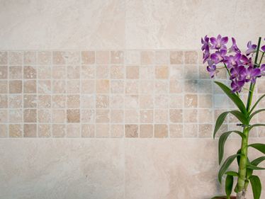 Orchidea na tle mozaikowej ściany z jasnego trawertynu