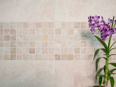 Orchidea na tle mozaikowej ściany z jasnego trawertynu