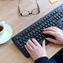 Ręce na klawiaturze, obok okulary i filiżanka kawy