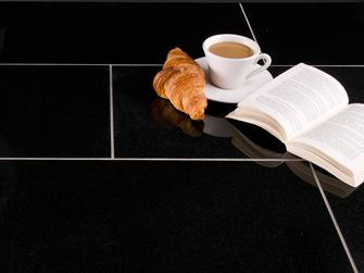 Ciemne płytki granitowe Nero Assoluto z rogalikiem, filiżanką kawy i otwartą książką