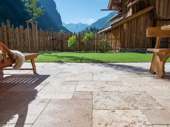 Podłoga tarasu z trawertynu Rustic i drewniane meble, w tle trawnik i widok na góry