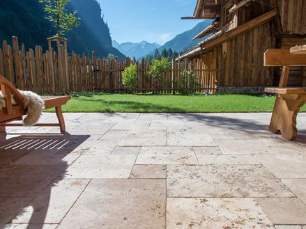 Podłoga tarasu z trawertynu Rustic i drewniane meble, w tle trawnik i widok na góry