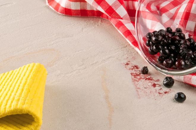 Żółta ściereczka, czerwona ściereczka kuchenna i szklana miska z wysypanymi jagodami na kamieniu naturalnym
