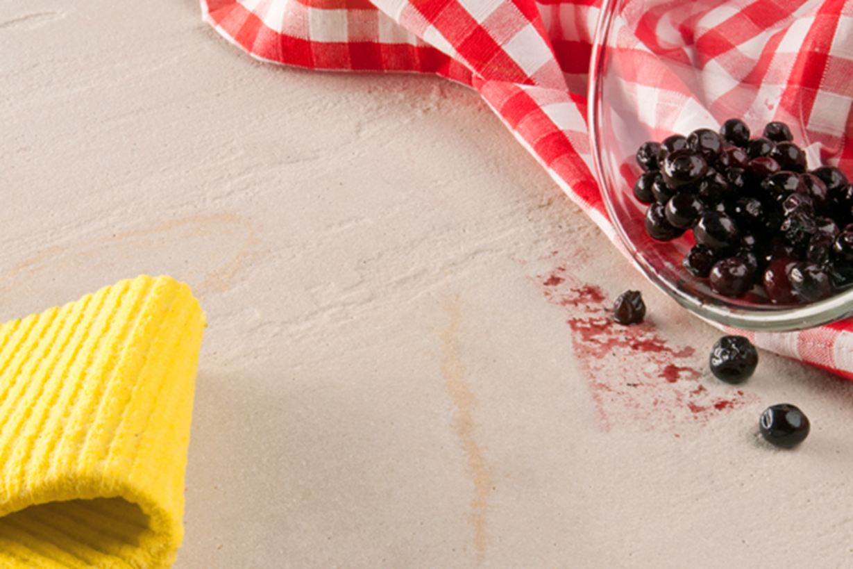 Żółta ściereczka, czerwona ściereczka kuchenna i szklana miska z wysypanymi jagodami na kamieniu naturalnym