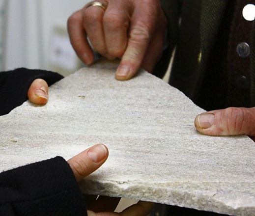 Dwie dłonie trzymają kawałek naturalnego kamienia z kwarcytu z Taunusu