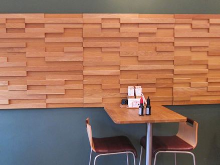 Stół z dwoma krzesłami przed szarą ścianą z brązowymi drewnianymi panelami w bistro